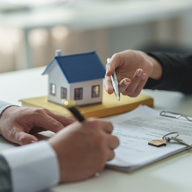 People signing real estate documents with a miniature house model, keys, and contract